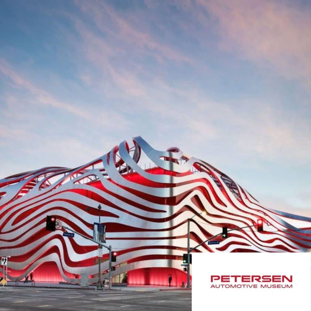 The Petersen Automotive Museum in Los Angeles, its red facade wrapped in curving ribbons of stainless steel against a sunset sky