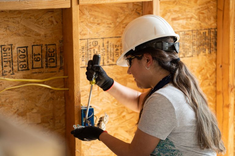 A Victor Valley College construction technology student in a hard hat and safety glasses working on a wall frame