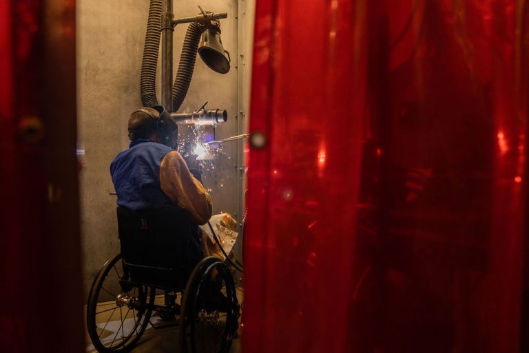 A Victor Valley College welding student at work in a welding booth behind a red safety curtain