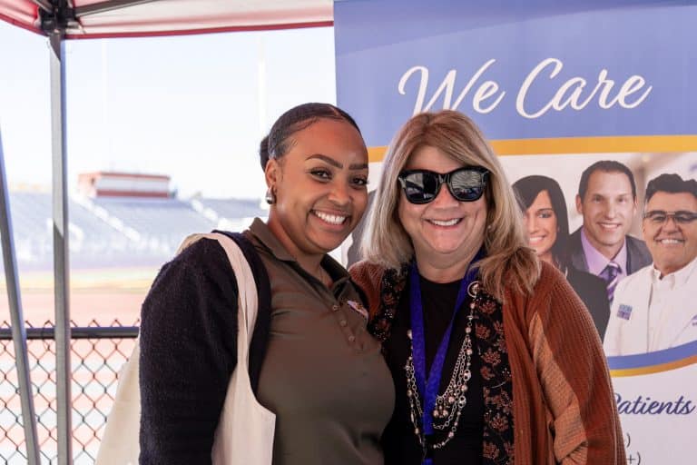 Two attendees smiling together at a community health exhibitor booth at the Summit