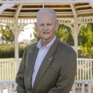 Portrait of Norm Hurst in a tweed jacket standing by a garden gazebo