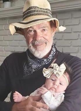 Portrait of David “Dave” Kniss wearing a straw fedora and holding his infant grandchild