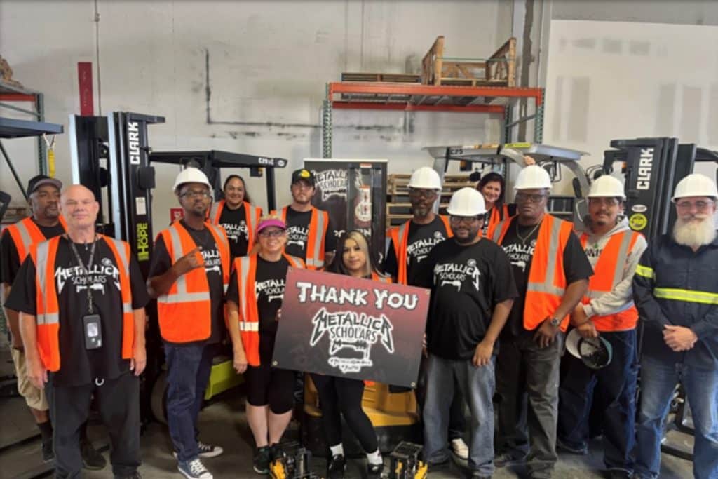 Victor Valley College Metallica Scholars in hi-vis vests and hard hats holding a Thank You Metallica Scholars sign beside forklifts in a training warehouse