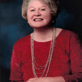 Portrait of Mary Helen Rolfes Brady, smiling in a red top with a pearl necklace