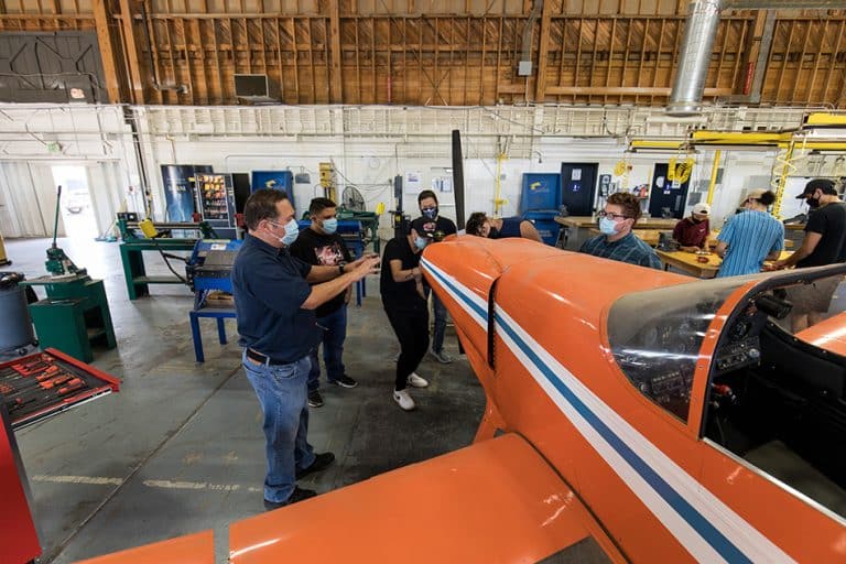 Victor Valley College aviation students gathered around a small orange aircraft in the hangar