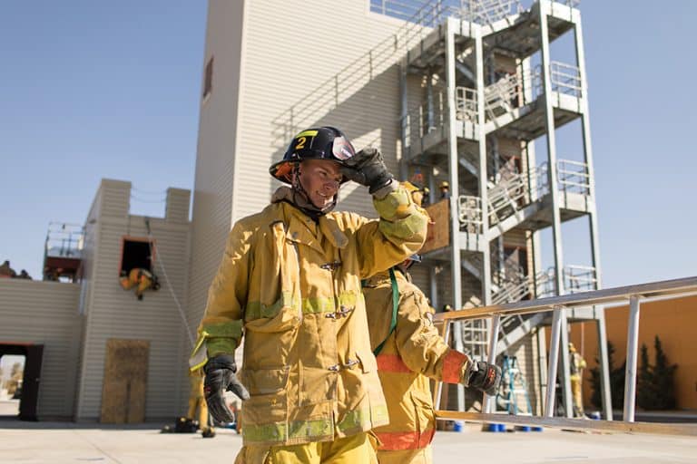 A Victor Valley College Fire Technology cadet in full turnout gear beside the training tower