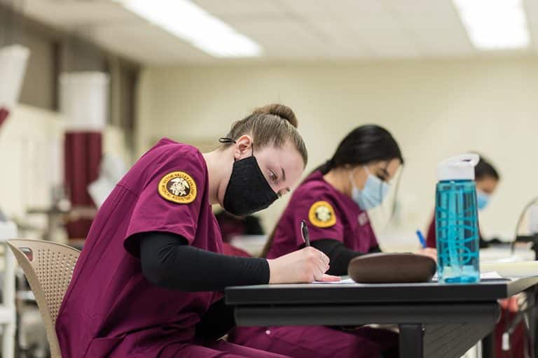 Victor Valley College nursing students in maroon scrubs taking notes during a class session