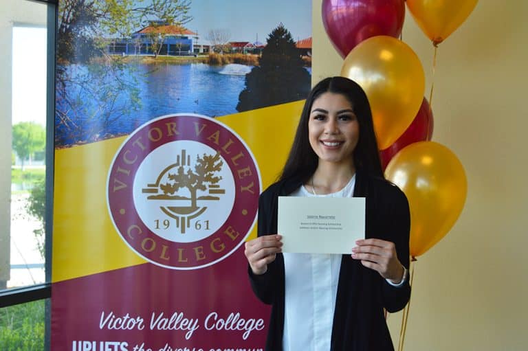 A Victor Valley College scholarship recipient holding her award certificate in front of the college seal